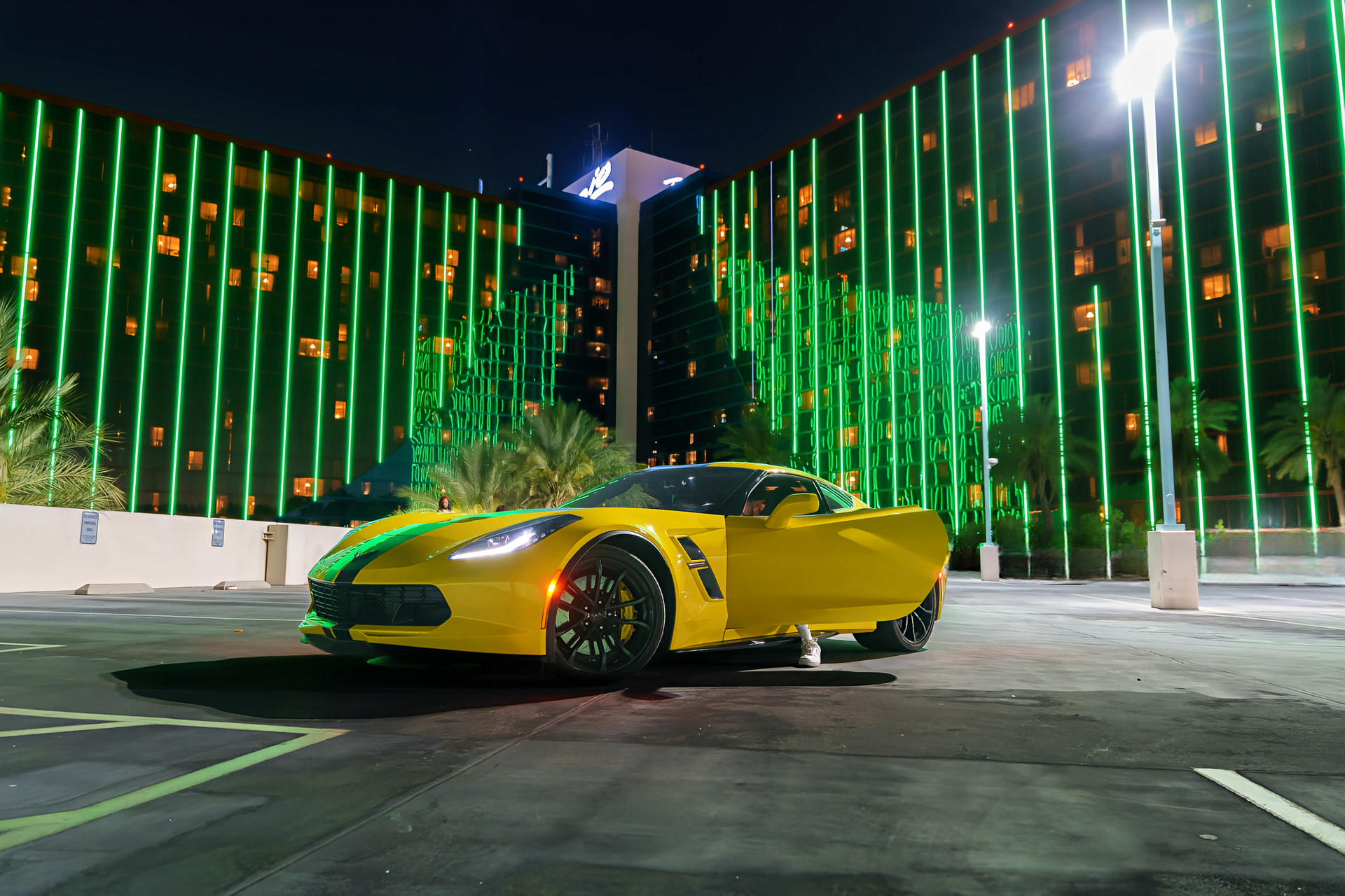 Yellow Chevrolet Corvette parked under green neon lights on the Las Vegas strip at night